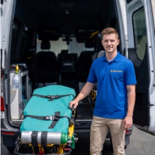 A man in a blue shirt stands beside a van, with an ambulance visible in the background.